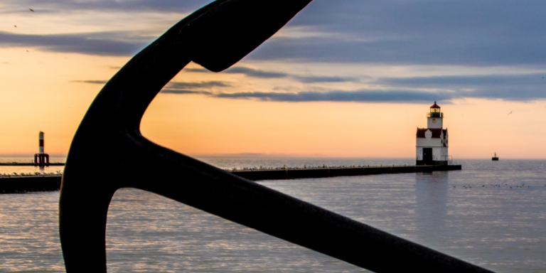 photo of two light houses in the background and an anchor in the foreground at sunset